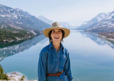 a woman wearing a hat standing in front of a lake